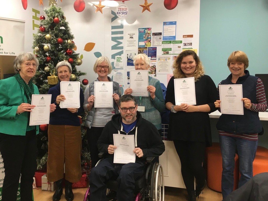 A group photo. Richard sits in his wheelchair in front of 6 volunteers. All are holding their certificates.