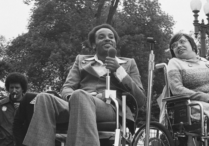A black man in a wheelchair holds a microphone