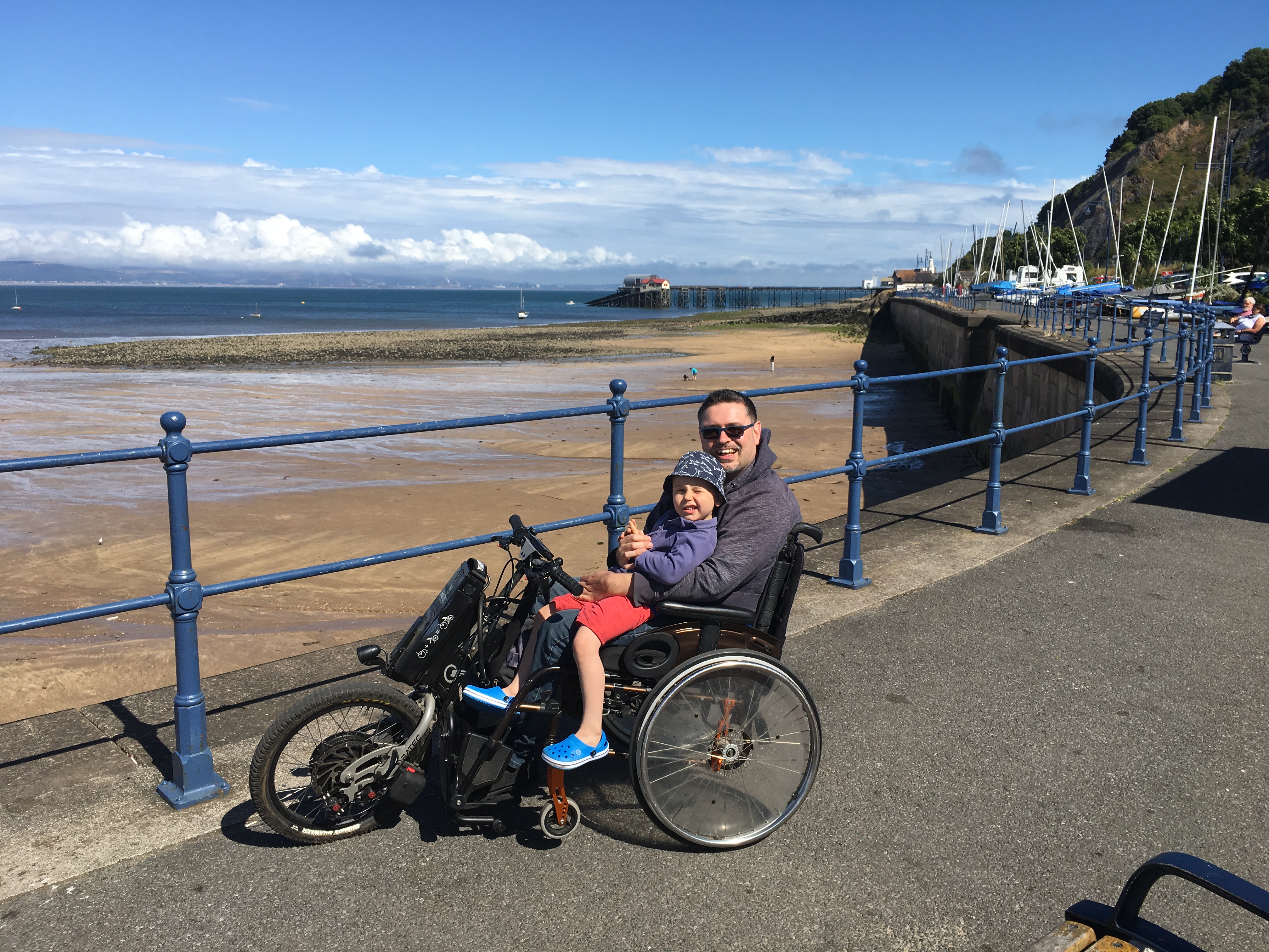 Richard on his Trike overlooking a sandy beach, Billy (nearly 4) sits on his lap
